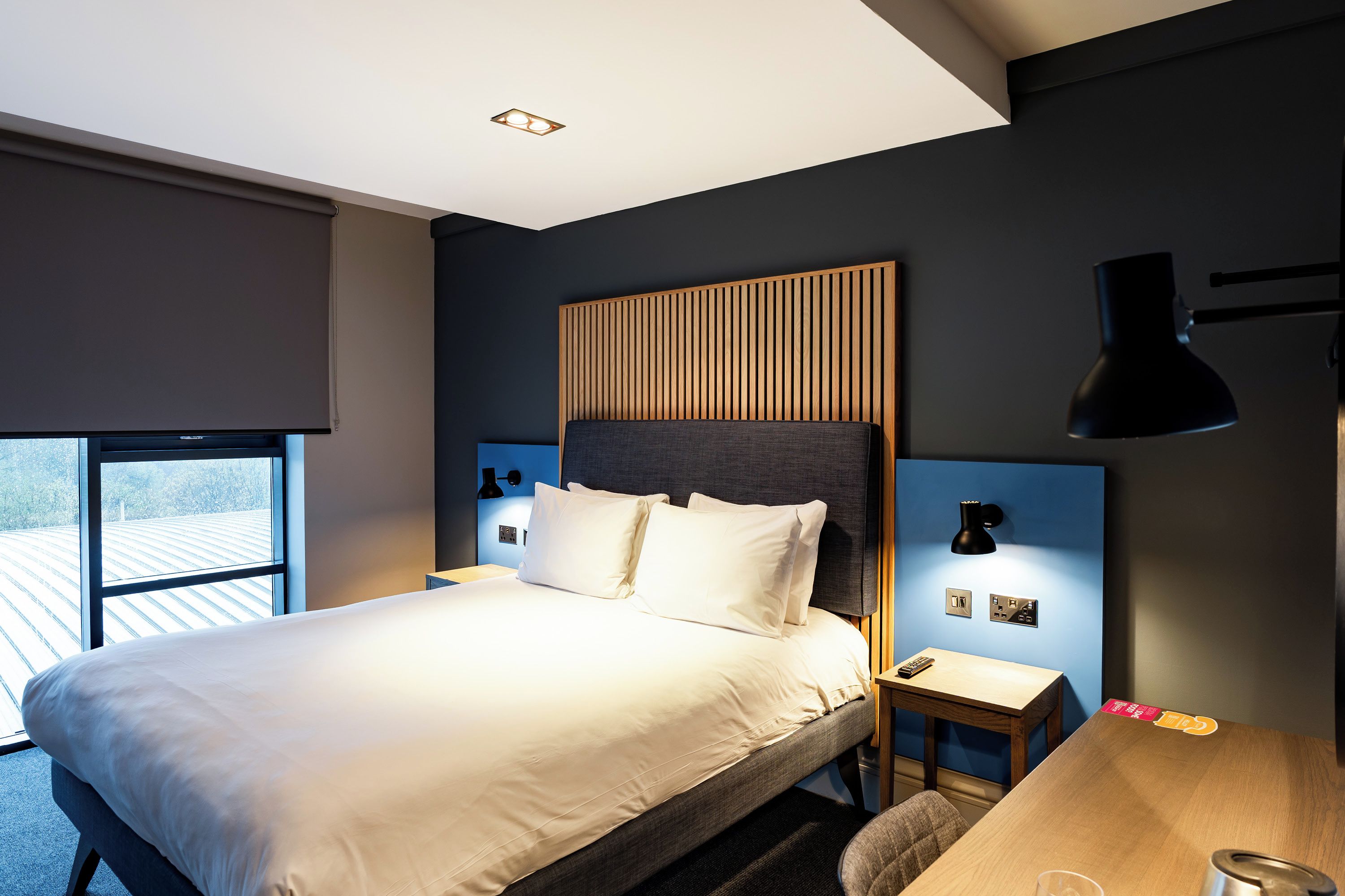 Ein modernes Hotelzimmer mit einem großen Bett, einem Schreibtisch, einem Sessel, einem Fenster mit Blick und einer Wandlampe.