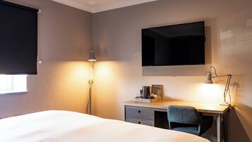 A hotel room with a bed, desk, chair, lamp, and a flat-screen TV mounted on the wall.