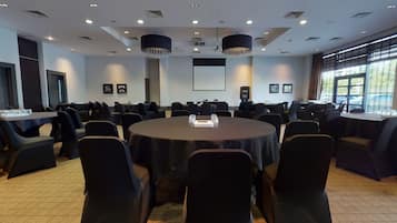 A conference room with round tables, black chairs, and a projector screen.