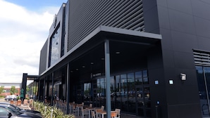 A modern building with a black facade, large windows, and outdoor seating area. - Village Hotel Leeds South (Leeds)