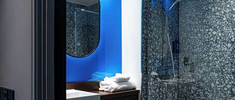 Un baño moderno con ducha de mármol, espejo redondo y lavamanos blanco.