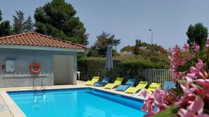 A swimming pool with lounge chairs, a lifebuoy, and a small building with a tiled roof. - Comfort Aparthotel Carcassonne (Carcassonne)