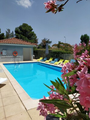 Une piscine avec des chaises longues, une bouée de sauvetage et un petit bâtiment doté d’un toit en tuiles.