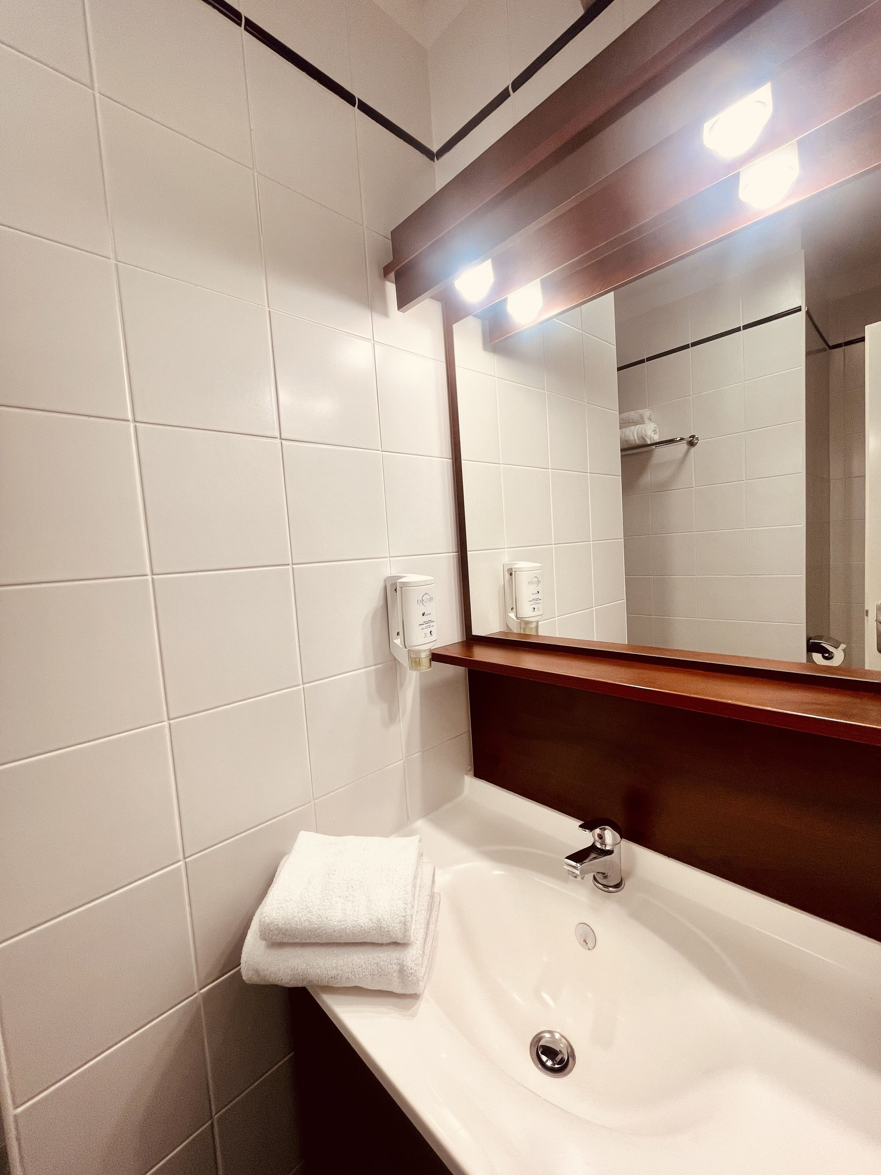 Une salle de bain avec des carreaux blancs, un lavabo, un miroir et un porte-serviettes.