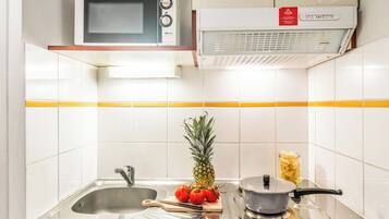 Een keuken met een magnetron, een fornuis, een spoelbak en een snijplank met tomaten en een ananas.
