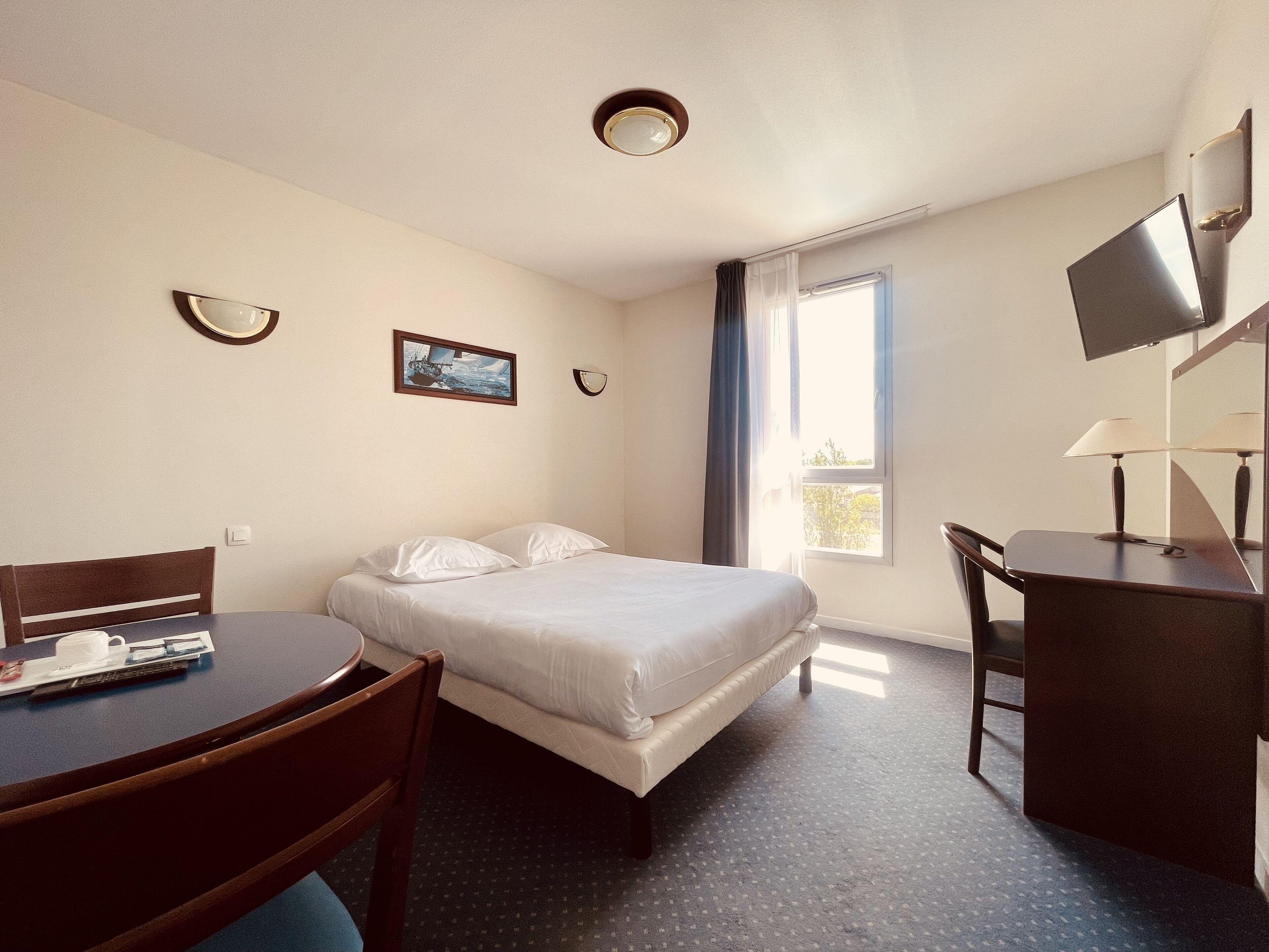 Ett hotellrum med en säng, ett skrivbord, en stol, en tv och ett fönster.