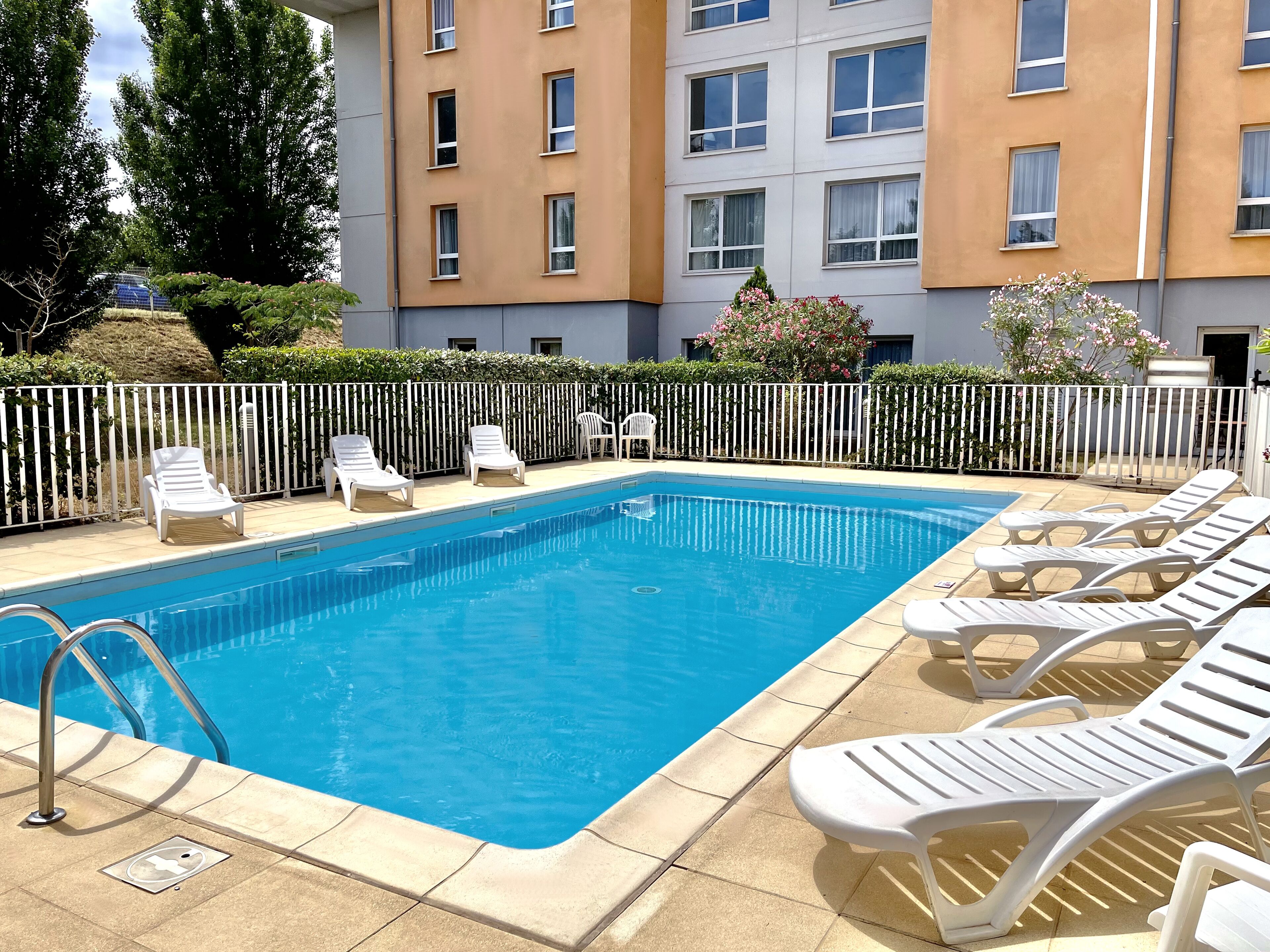 A rectangular swimming pool with a metal ladder, surrounded by a white fence.