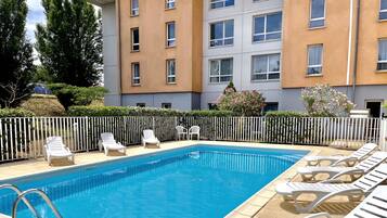 A rectangular swimming pool with a metal ladder, surrounded by a white fence.