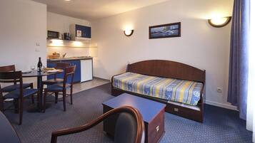 Quarto de hotel compacto com cama, pequena mesa de escritório, cadeira, mesa e cozinha compacta.