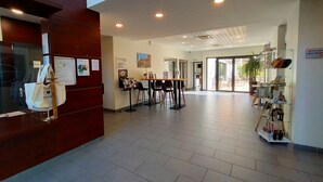 A reception area with a wooden reception desk, a glass display case with shoes, and a seating area with chairs and a table. - Comfort Aparthotel Carcassonne (Carcassonne)