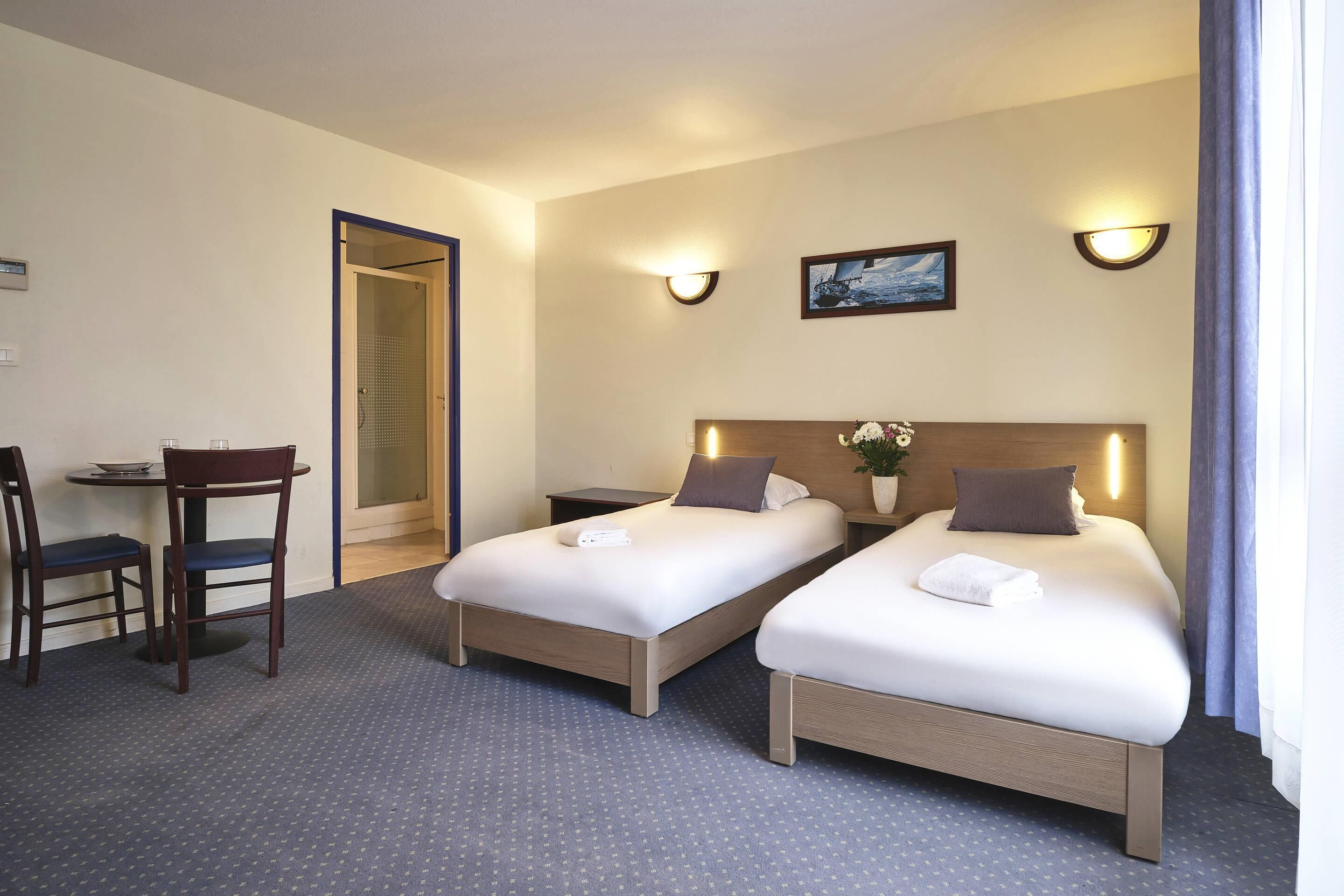 Una habitación de hotel con dos camas individuales, un escritorio pequeño con una silla y una mesita de noche.