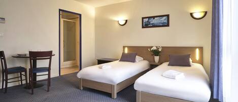 Quarto de hotel com duas camas de solteiro, uma pequena escrivaninha com cadeira e mesa de cabeceira.