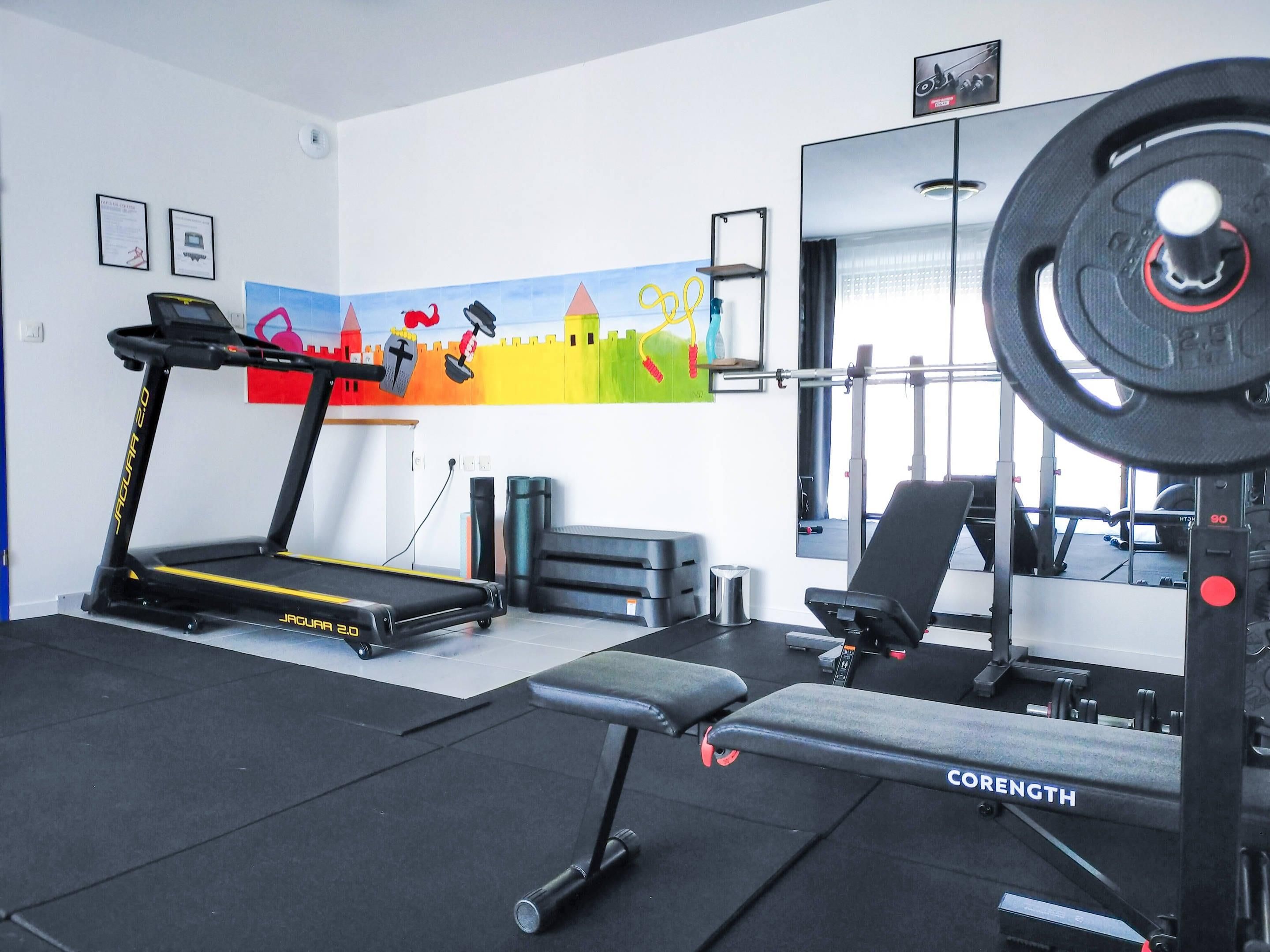A gym with a treadmill, weight bench, and a mirror.