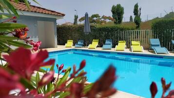 Una piscina con sillones de descanso, techo de baldosas y un seto al fondo.