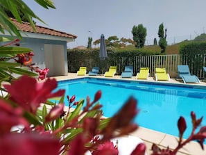 Una piscina con sillones de descanso, techo de baldosas y un seto al fondo.