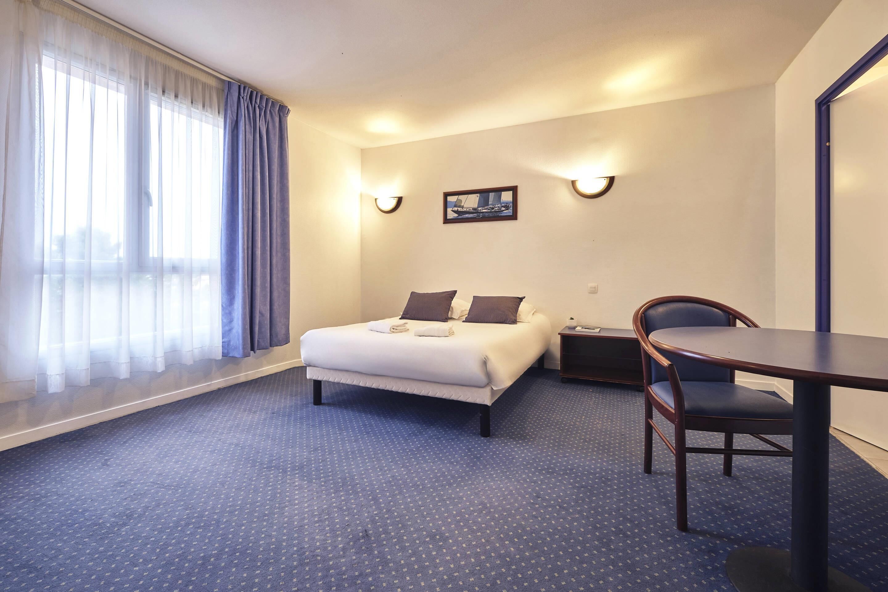 Ein Hotelzimmer mit einem Bett, einem Schreibtisch und einem Stuhl. Zwei Wandleuchten und ein gerahmtes Bild sind an der Wand angebracht.