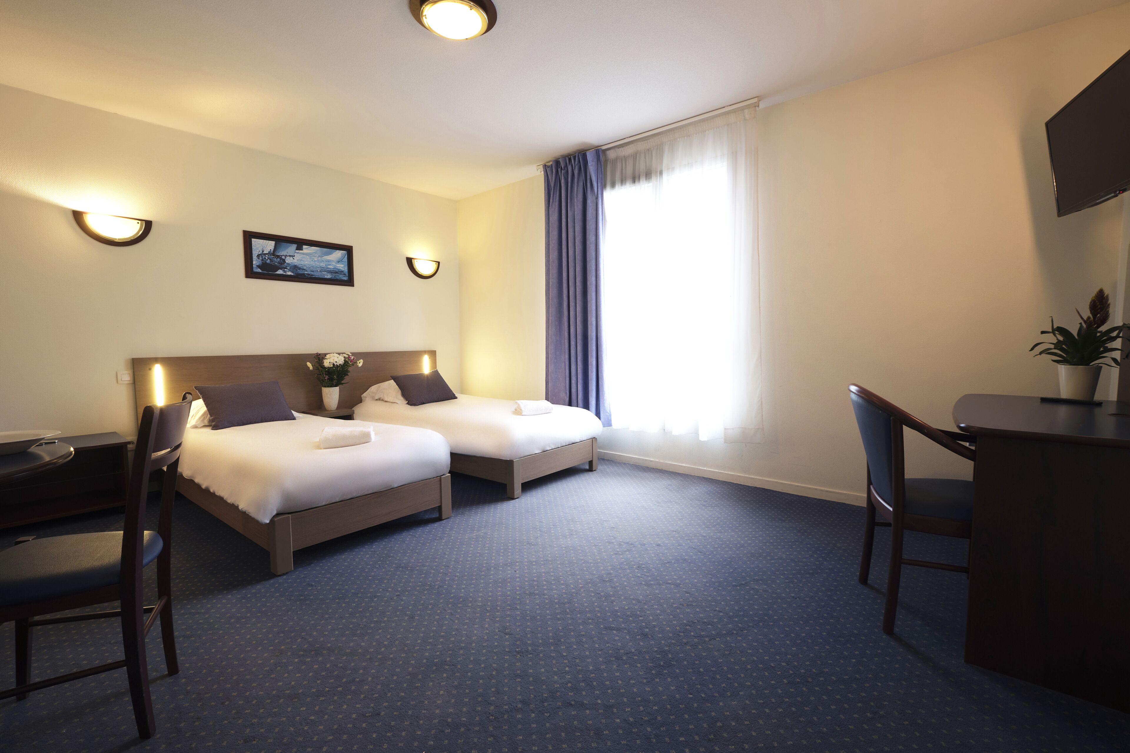 Une chambre d’hôtel avec deux lits, un bureau, une chaise, une télévision et une fenêtre avec des rideaux.