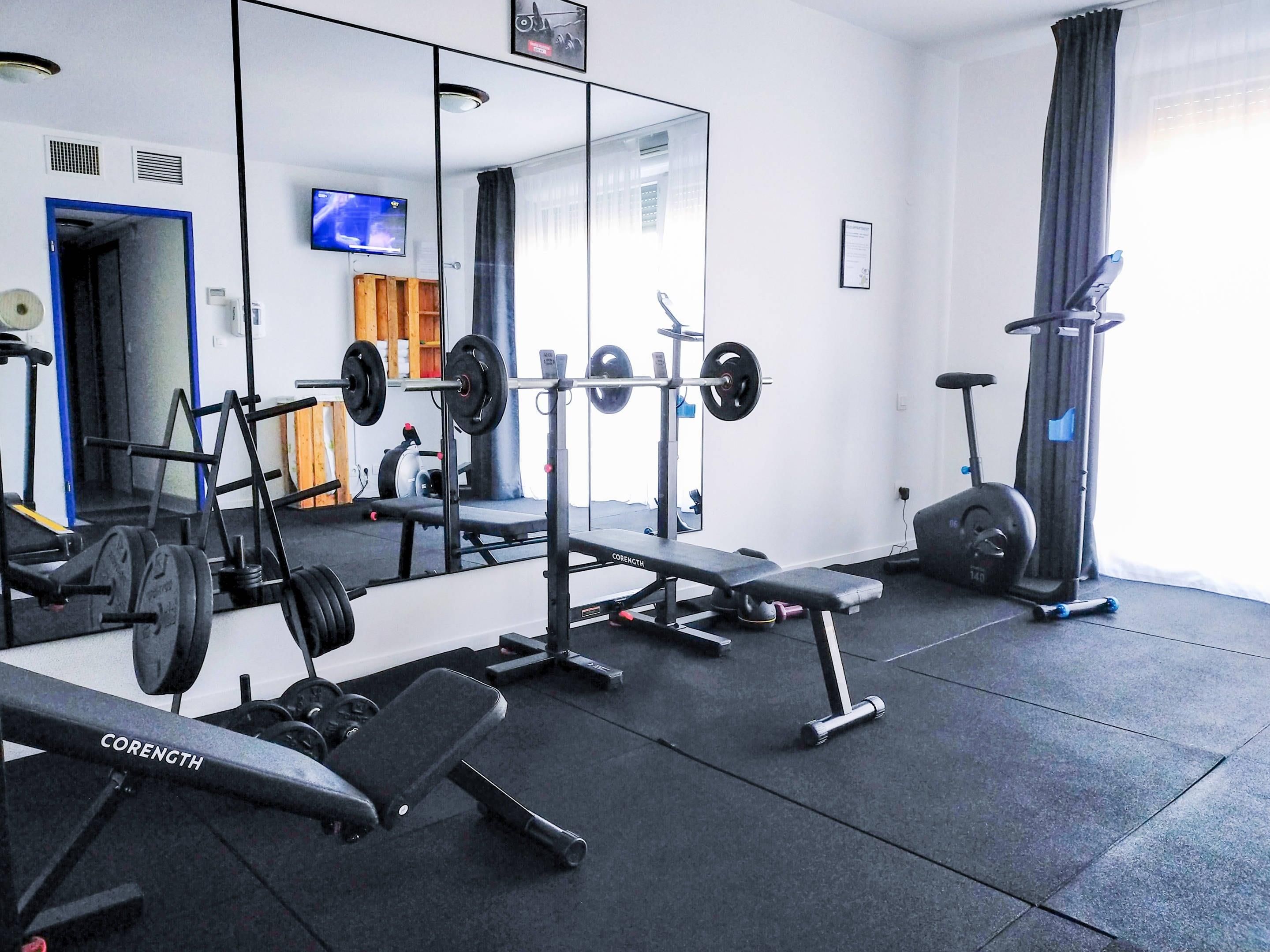 A gym with weightlifting equipment, a bench, and a mirrored wall.