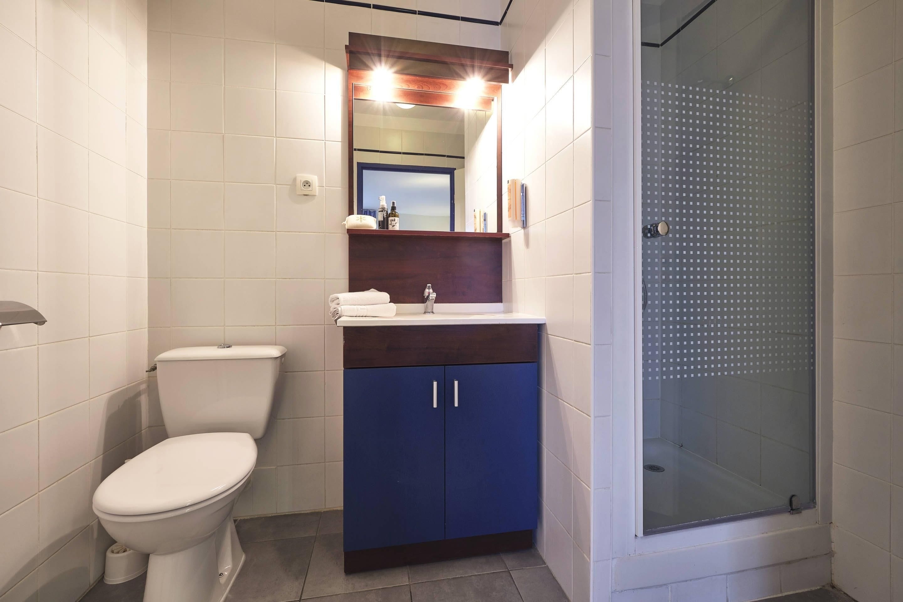 Un baño con inodoro, lavabo con espejo y ducha con puerta de cristal.