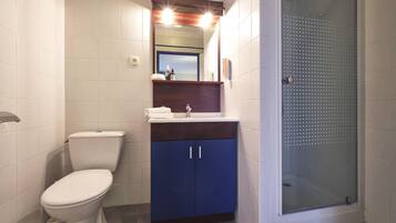 Un baño con inodoro, lavabo con espejo y ducha con puerta de cristal.