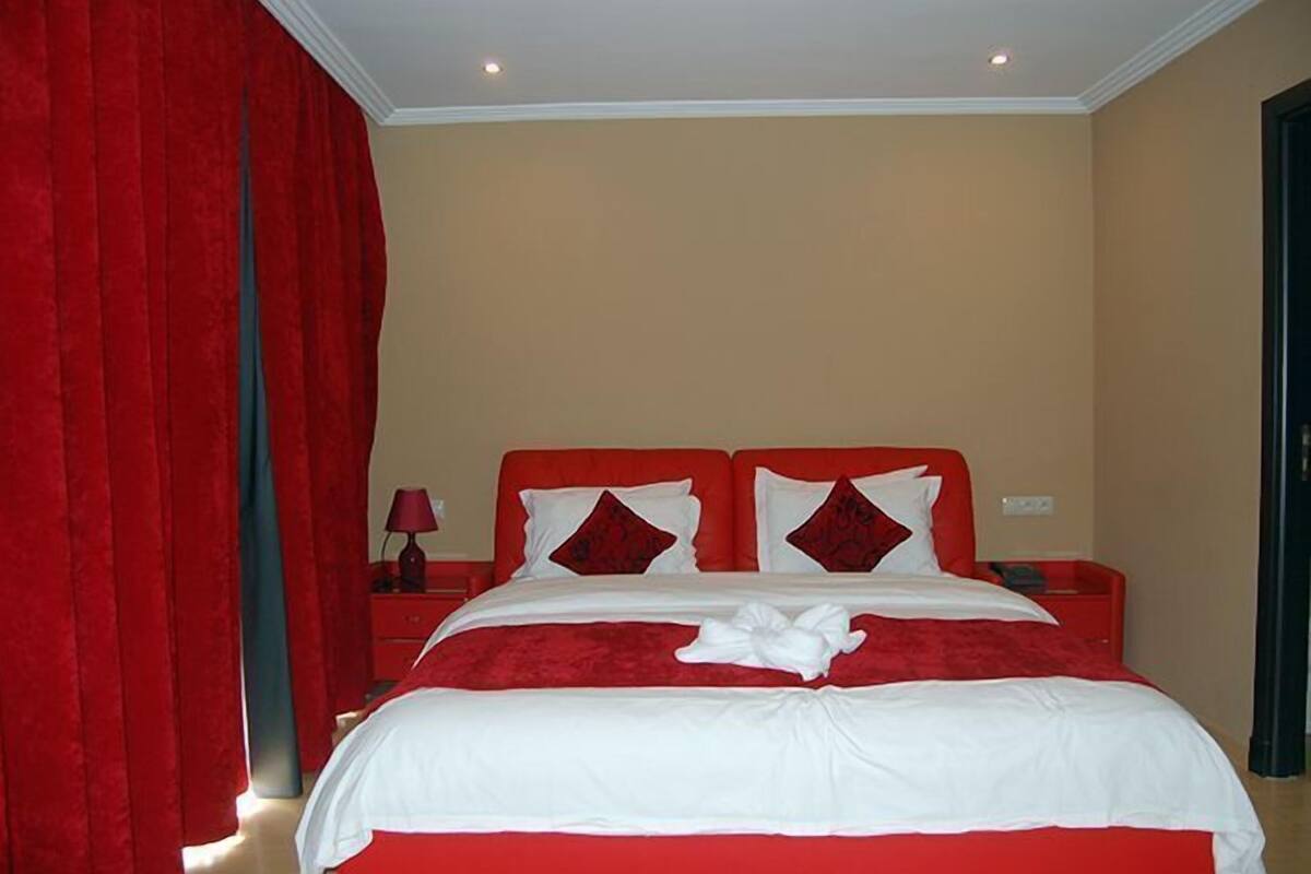 Ein Hotelzimmer mit einem großen Bett, roten Vorhängen, einem Nachttisch mit Lampe und einem roten Kopfteil.