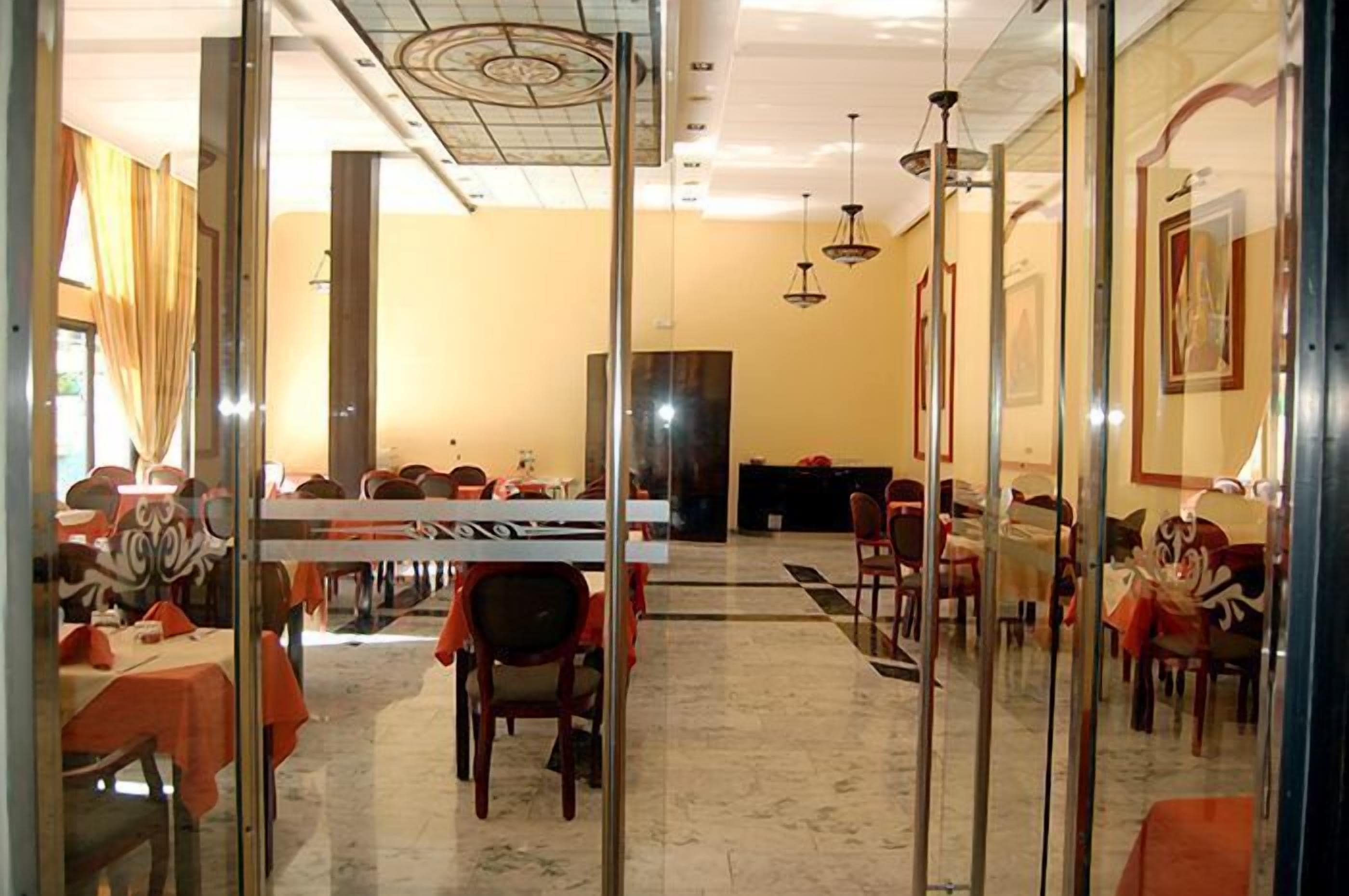 A restaurant with glass partitions, tables with orange tablecloths, and hanging pendant lights.