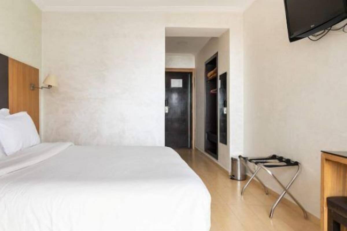 Ein Hotelzimmer mit einem großen Bett, einem Holzkopfende, einem flachbildfernseher an der Wand und einem Gang zu weiteren Zimmern.