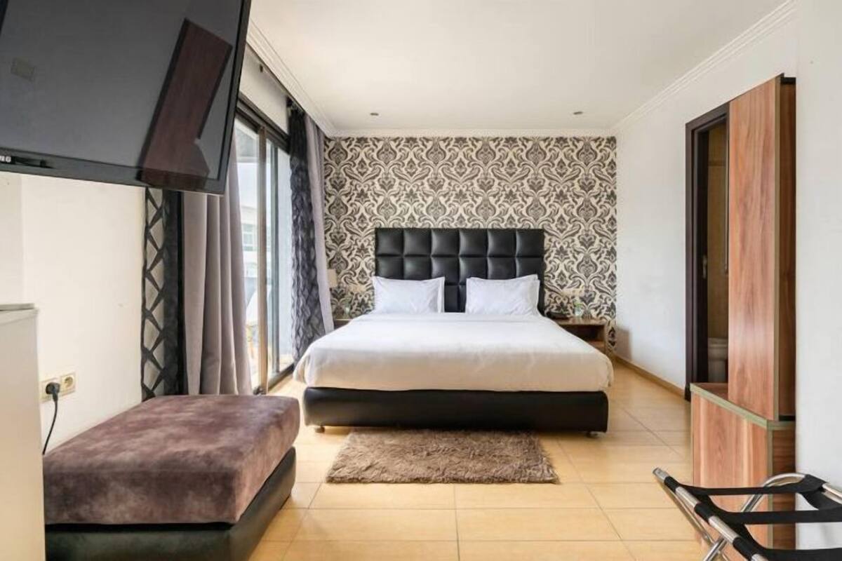Ein Schlafzimmer mit einem großen Bett, einer kleinen Bank, einem Fernseher und einem Kleiderschrank.