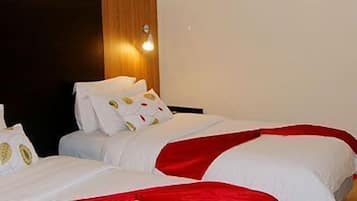 Une chambre d’hôtel avec deux lits, chacun agrémenté de draps blancs et de touches de couleur rouge, un plancher en bois et un luminaire fixé au mur.