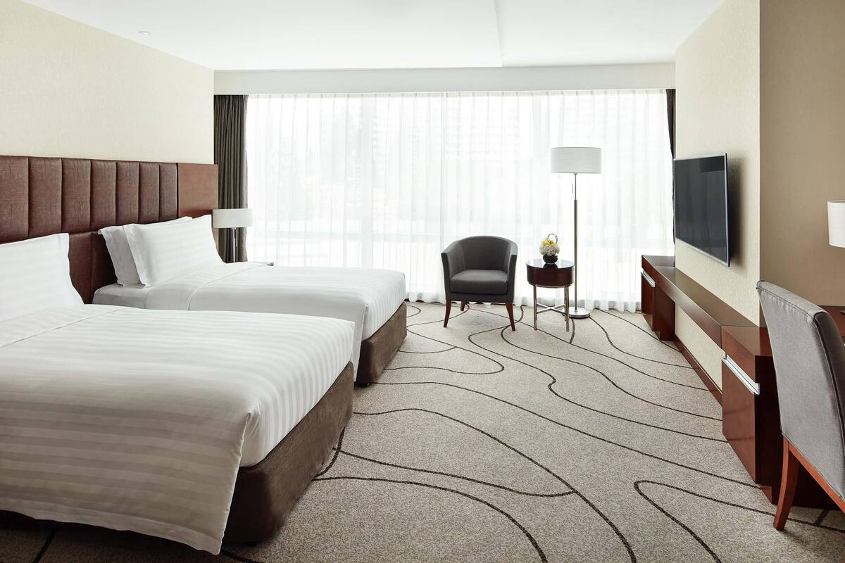 Habitación de hotel con dos camas, una silla, un televisor y un escritorio con lámpara.