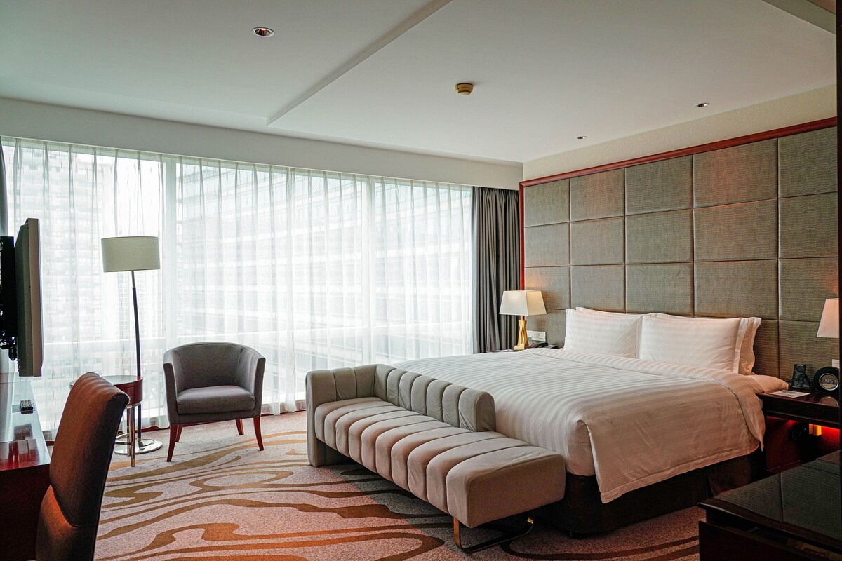 Una habitación de hotel moderna con una cama grande, una zona de estar, un escritorio y un televisor.