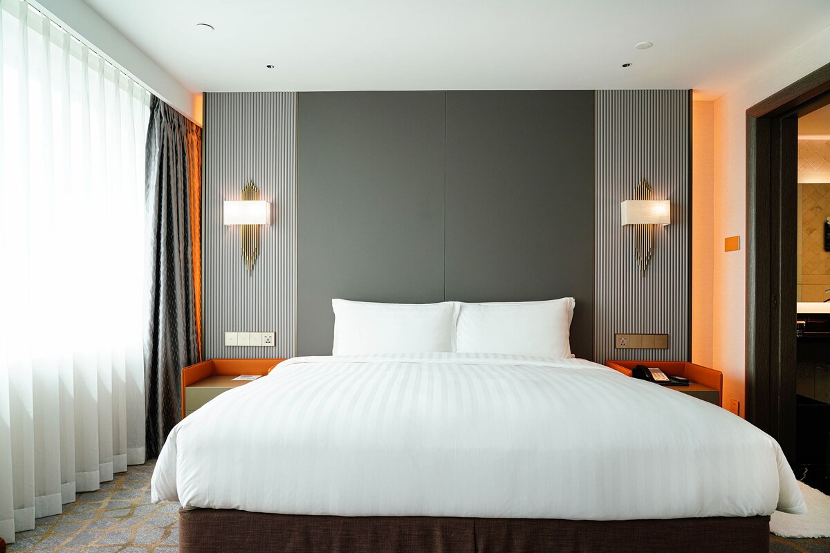 Una habitación de hotel con una cama grande, dos mesitas de noche, una lámpara de pared y una ventana con cortinas.