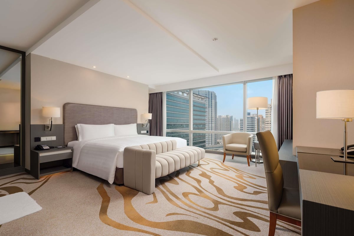 Una habitación de hotel moderna con una cama grande, un escritorio, una silla y vistas a la ciudad.