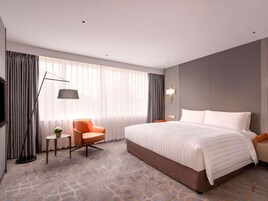 A hotel room with a large bed, a chair, a small table, and a TV.