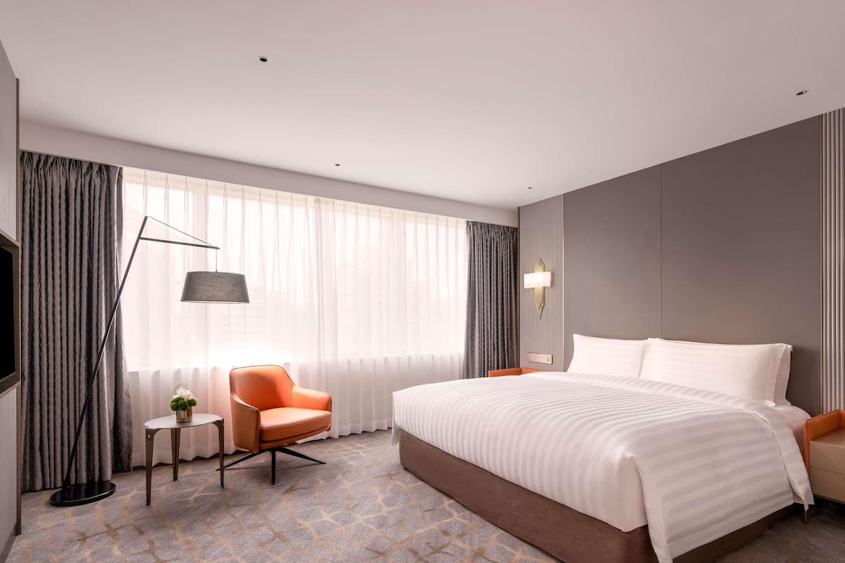Una habitación de hotel moderna con una cama grande, una silla, una mesita y un televisor.