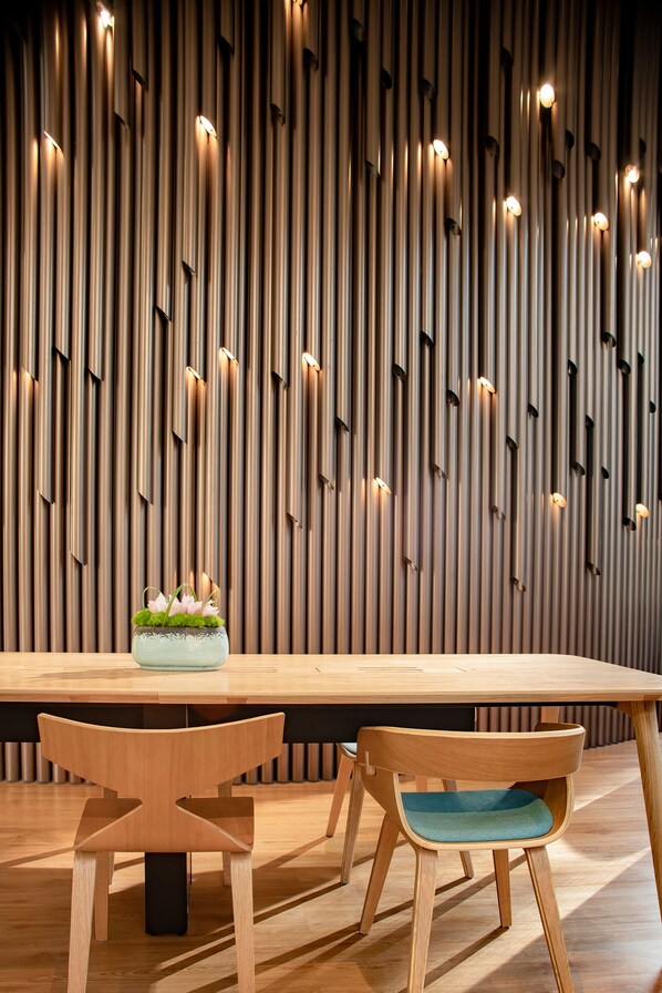 A modern dining area with a wooden table and chairs, a decorative centerpiece, and a wall with vertical slats and integrated lighting. - Pullman Shanghai Central-in XinTianDi & Yu Garden Area (Shanghai)