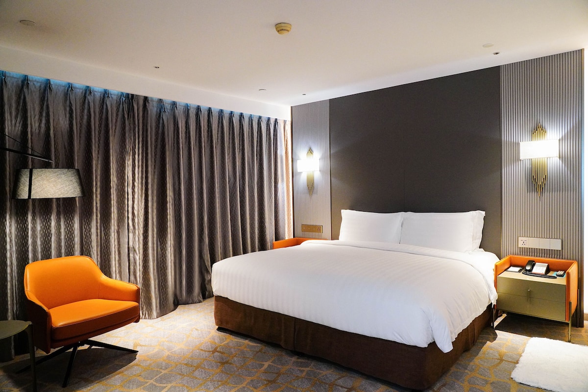 Una habitación de hotel moderna con una cama grande, un sofá, una mesita de noche y una lámpara.