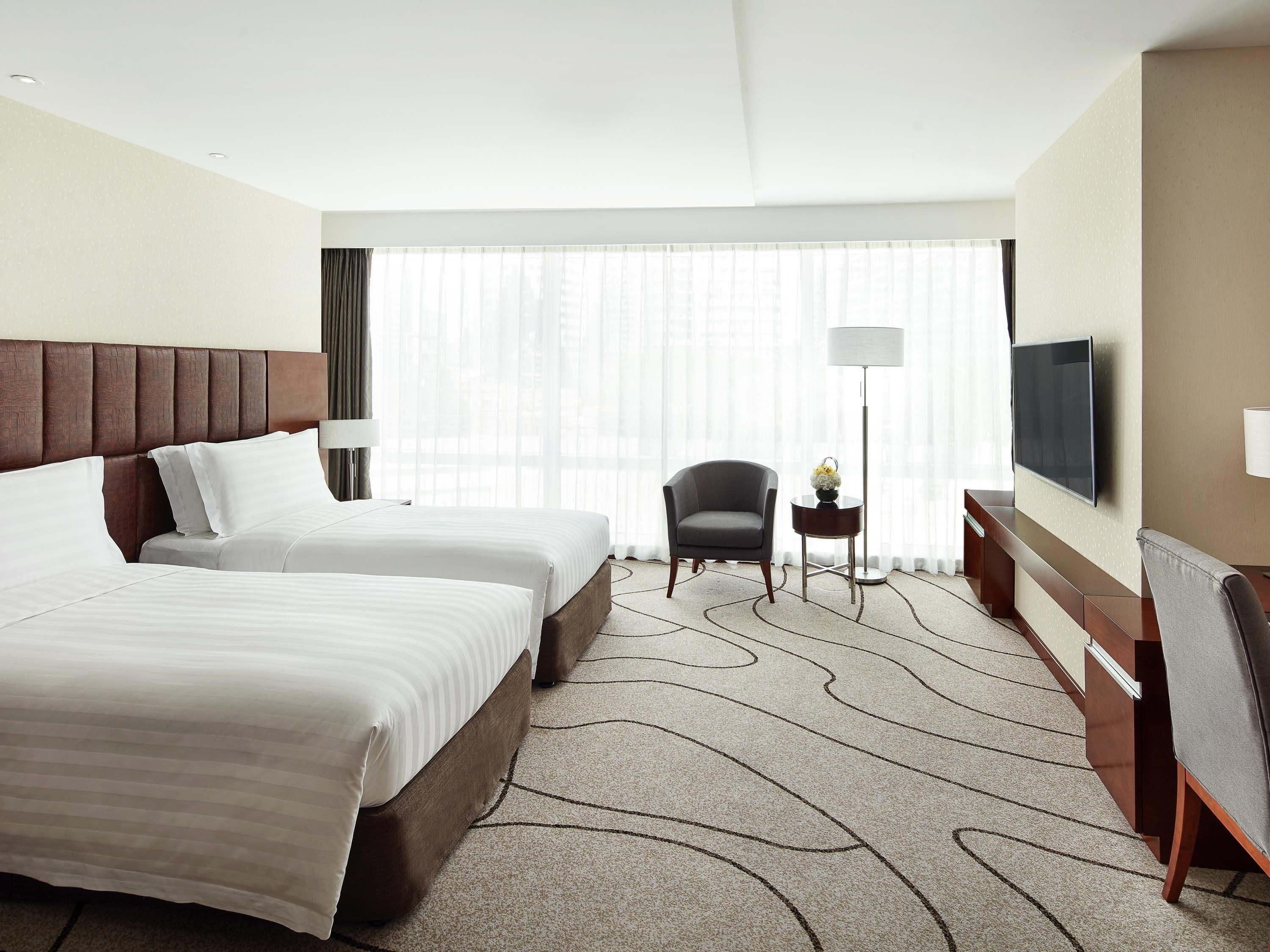 Habitación de hotel con dos camas, una silla, un televisor y un escritorio con lámpara.