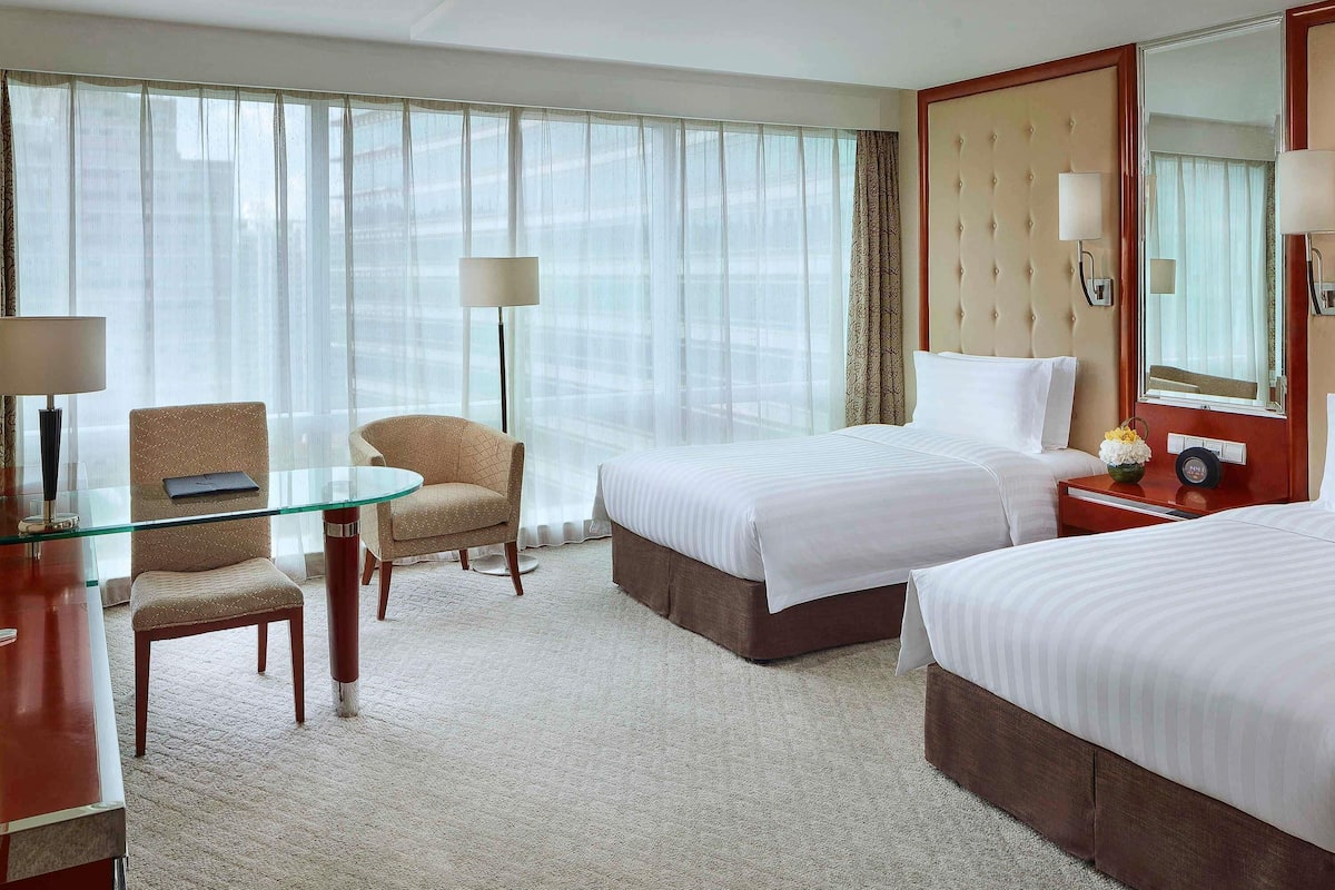 Habitación de hotel con dos camas, una mesa de vidrio, una silla, una lámpara y un espejo grande.