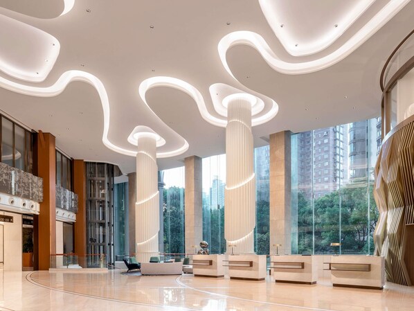A modern lobby with a reception desk, seating area, and large windows offering a view of the city. - Pullman Shanghai Central-in XinTianDi & Yu Garden Area (Shanghai)