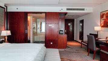 A hotel room with a bed, desk, chair, and a bathroom visible through an open door.