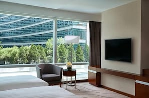 A hotel room with a large bed, a chair, a small table with a vase, a flat-screen TV, and a view of a modern building and trees. - Pullman Shanghai Central-in XinTianDi & Yu Garden Area (Shanghai)