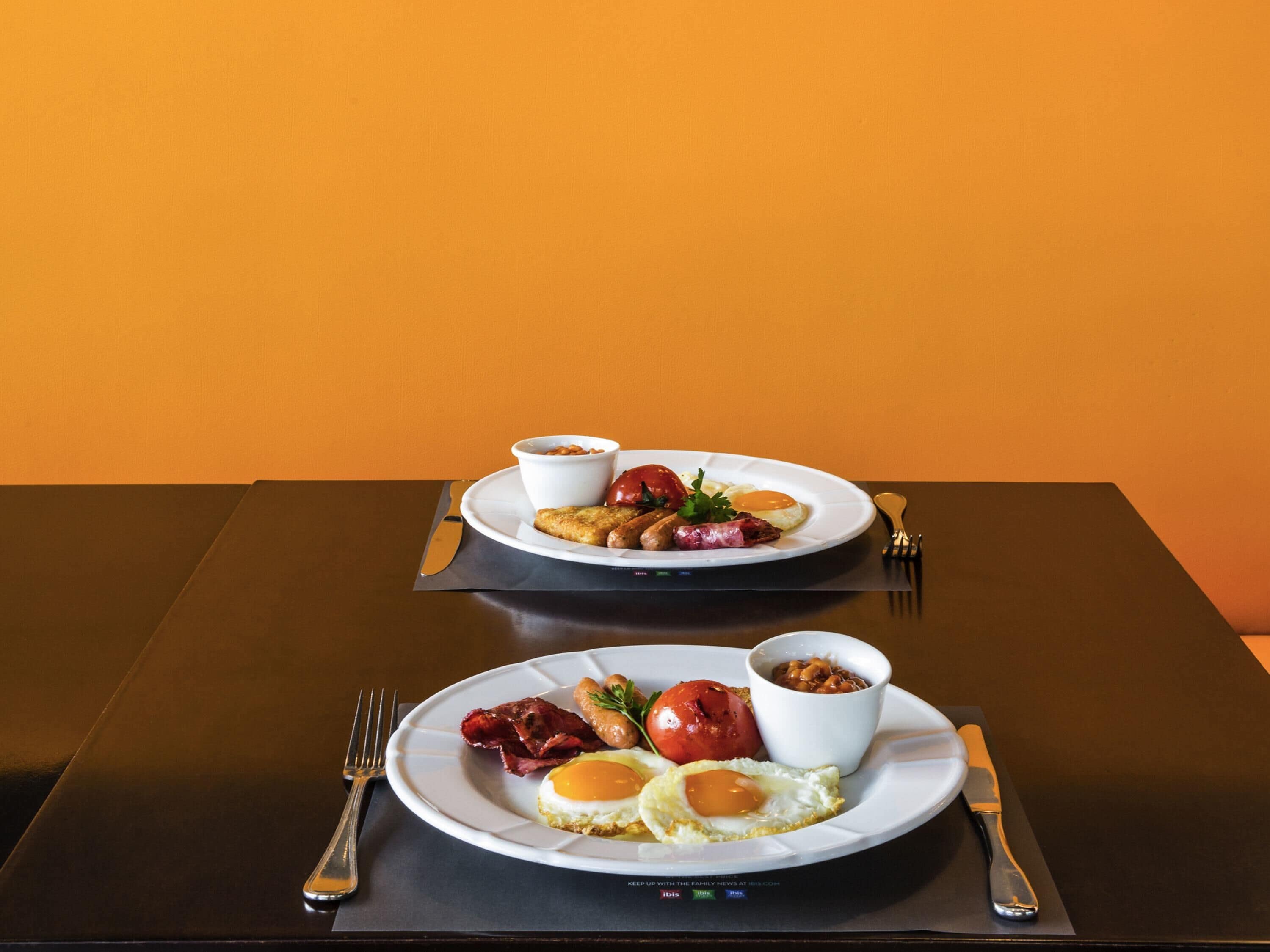 Deux assiettes remplies de nourriture pour le petit-déjeuner sont posées sur une table recouverte d’une nappe noire et agrémentée d’un set de table marron.