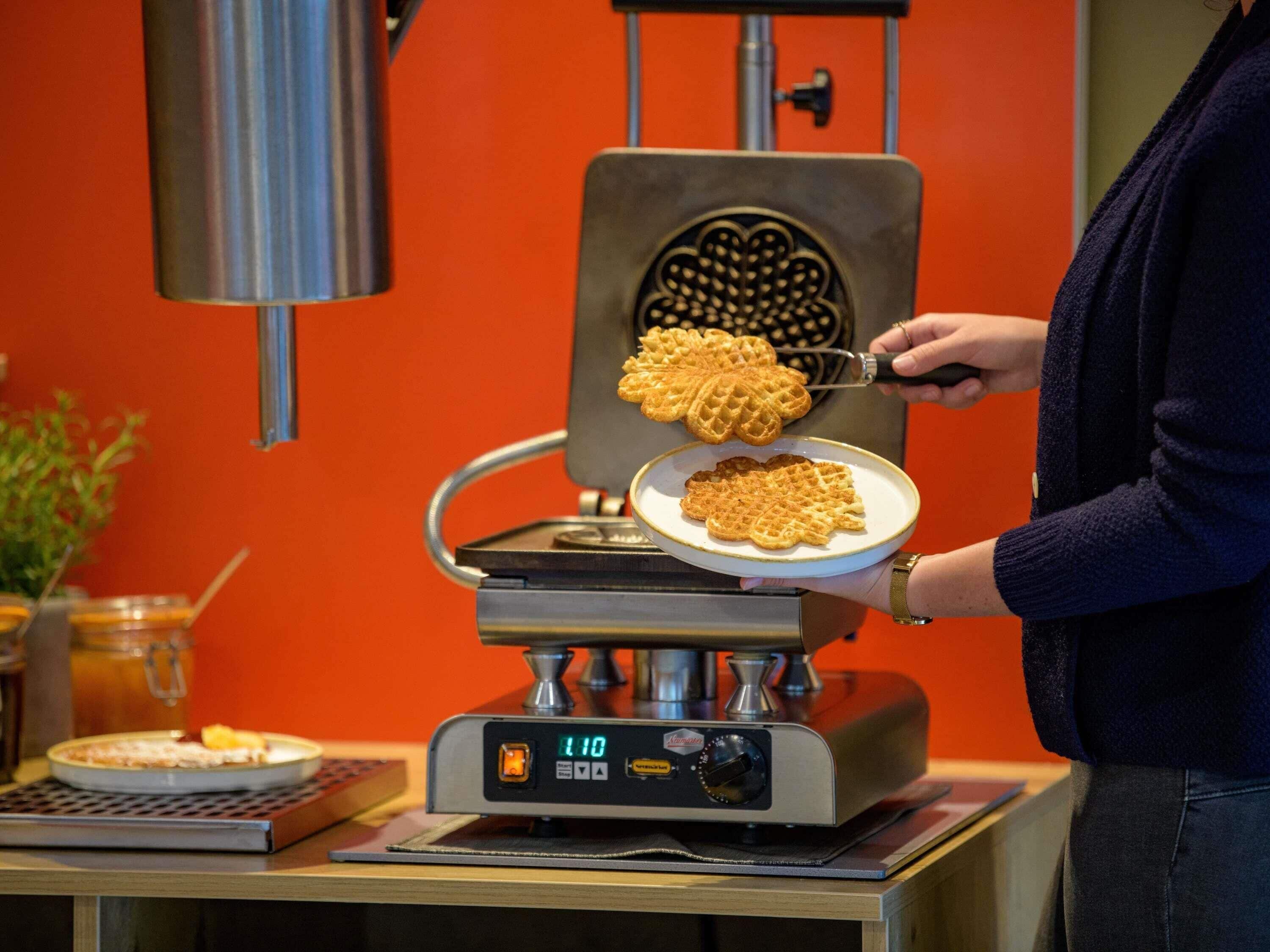 A waffle iron with waffles being removed, a digital display, and a person wearing a dark sweater.