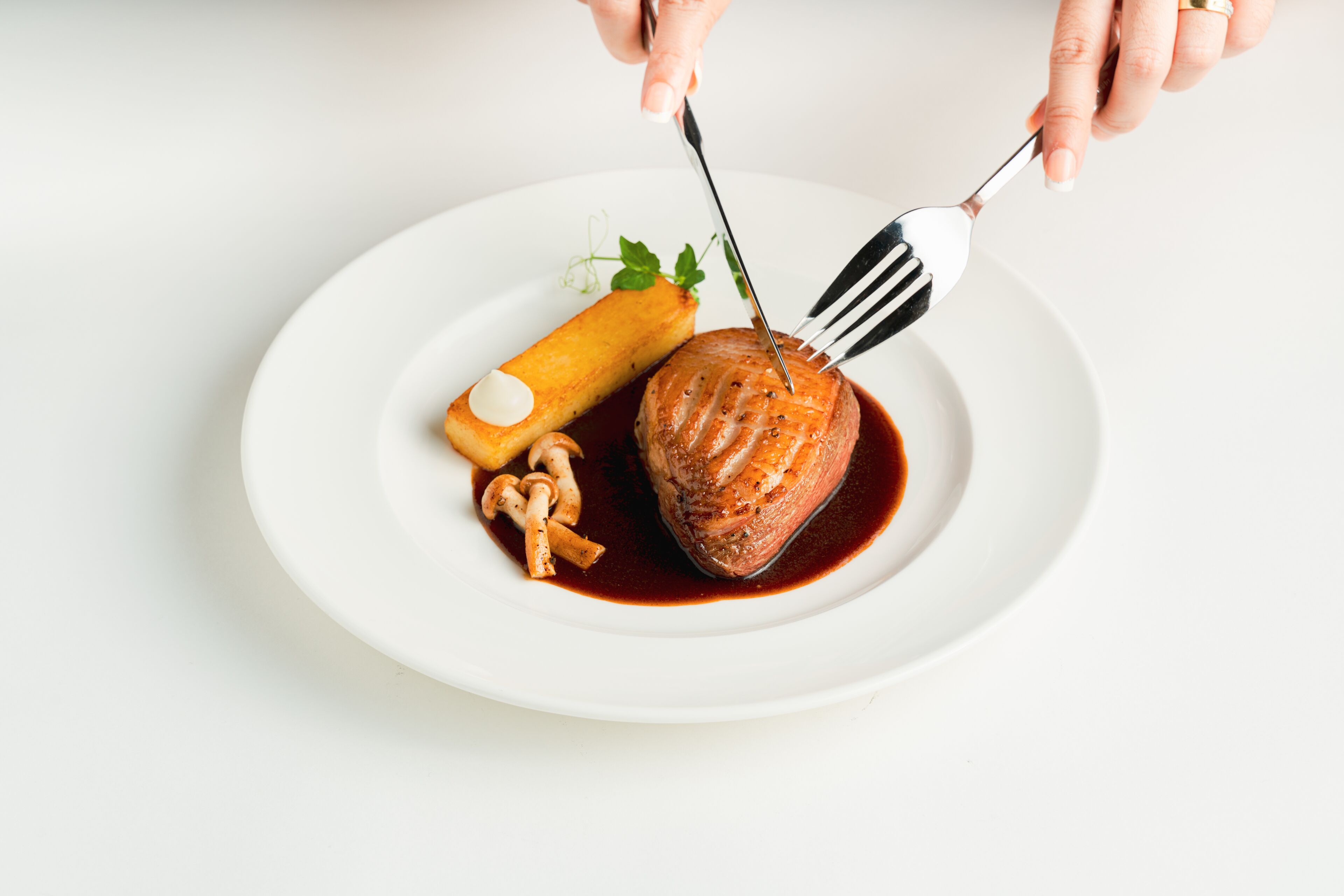 A white plate with a piece of meat, a small round item, and some mushrooms.