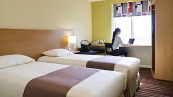 Une chambre d’hôtel avec deux lits, un bureau avec un ordinateur portable, un téléphone et une fenêtre avec des rideaux.