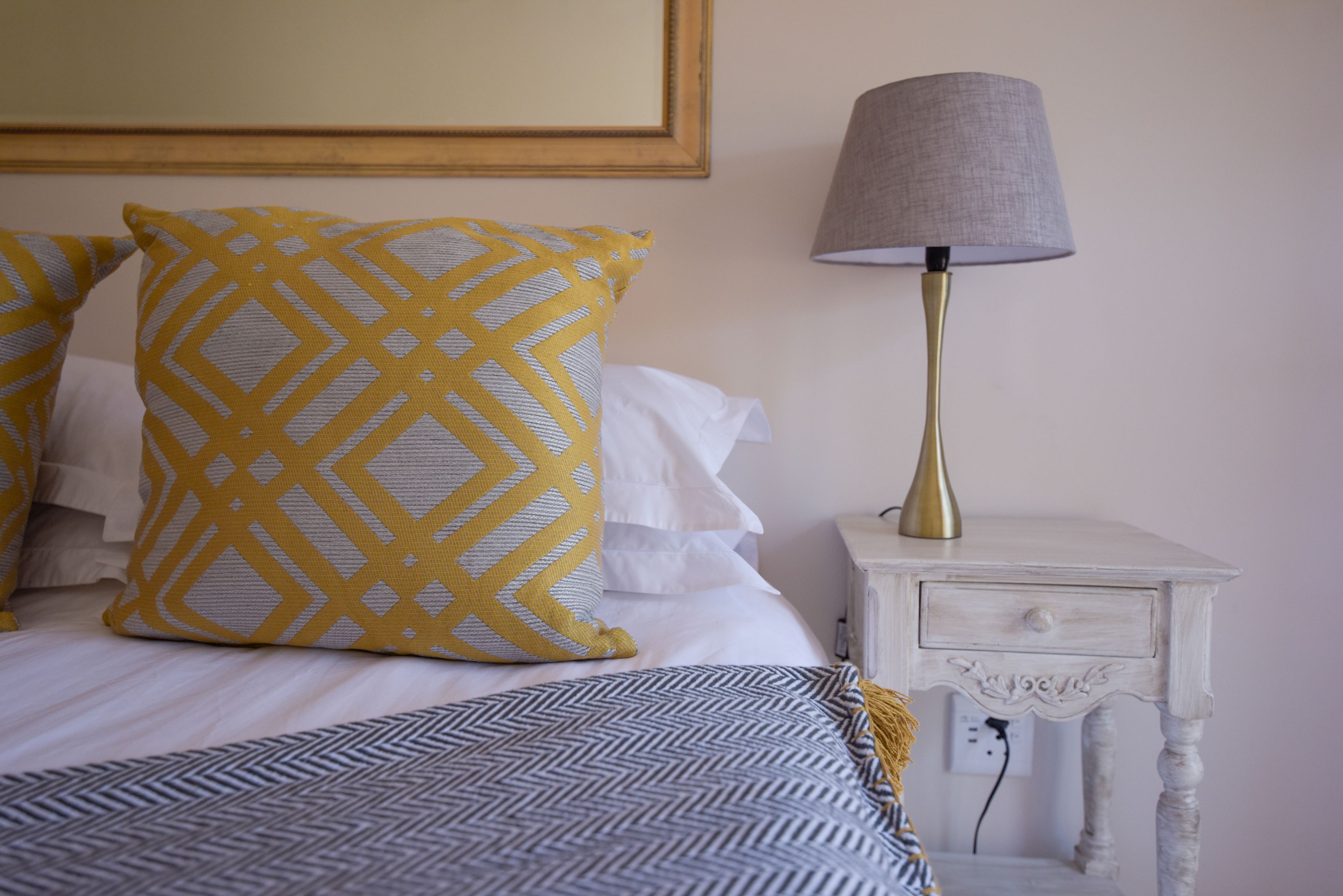 A neatly made bed with patterned pillows, a bedside lamp, and a small white nightstand with a drawer.