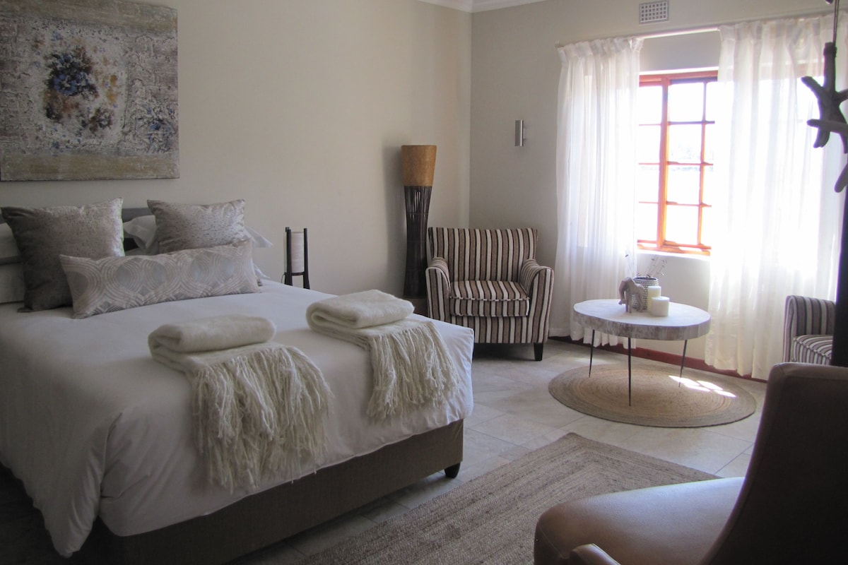 A bedroom with a large bed, a chair, a small table, and a window with curtains.