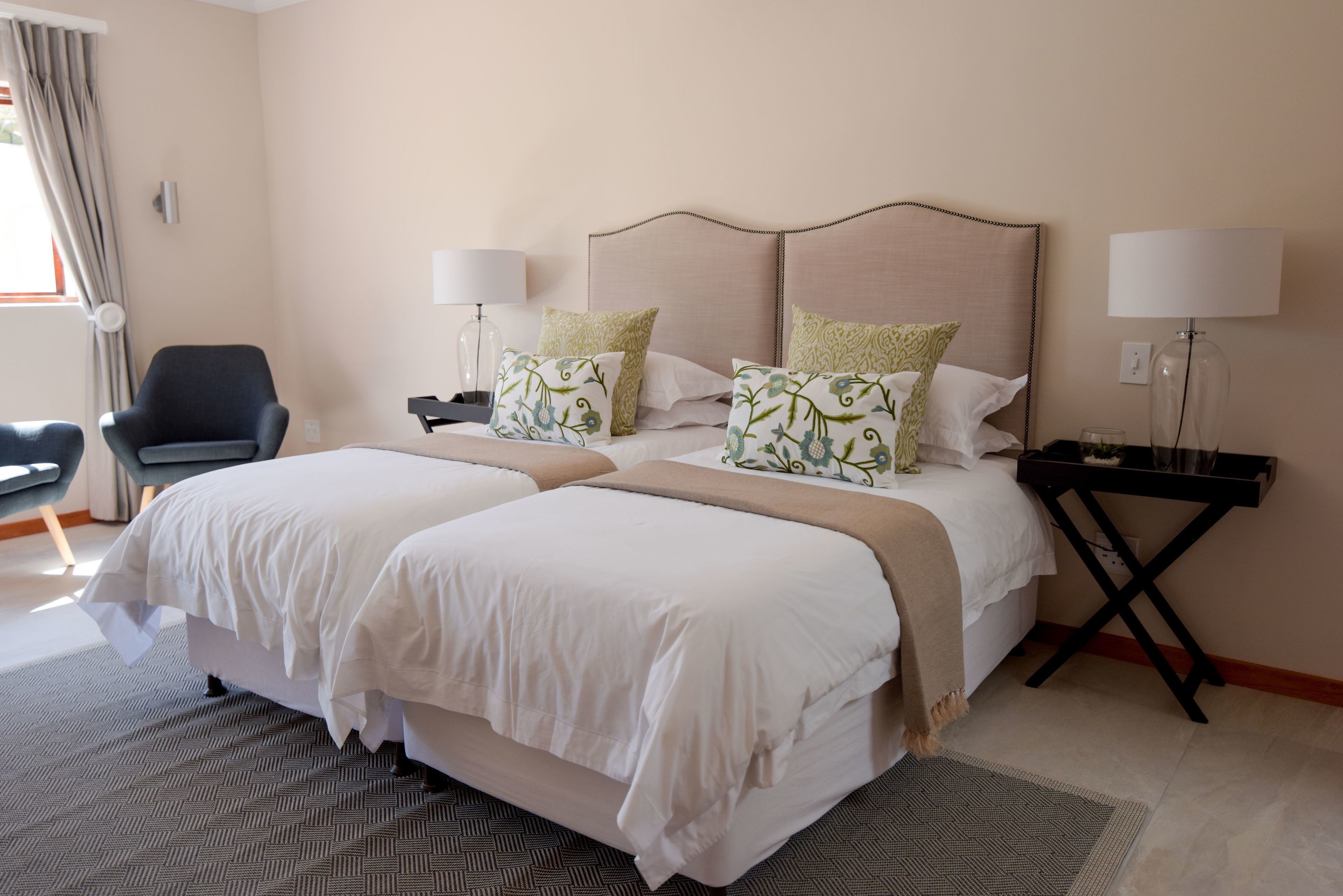 A hotel room with two beds, a chair, lamps, and a desk.