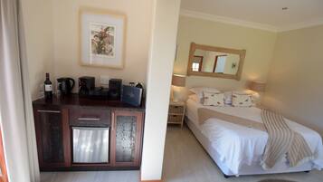 Habitación de hotel con cama, mesita de noche y un área de kitchenette con cafetera y botella de vino.